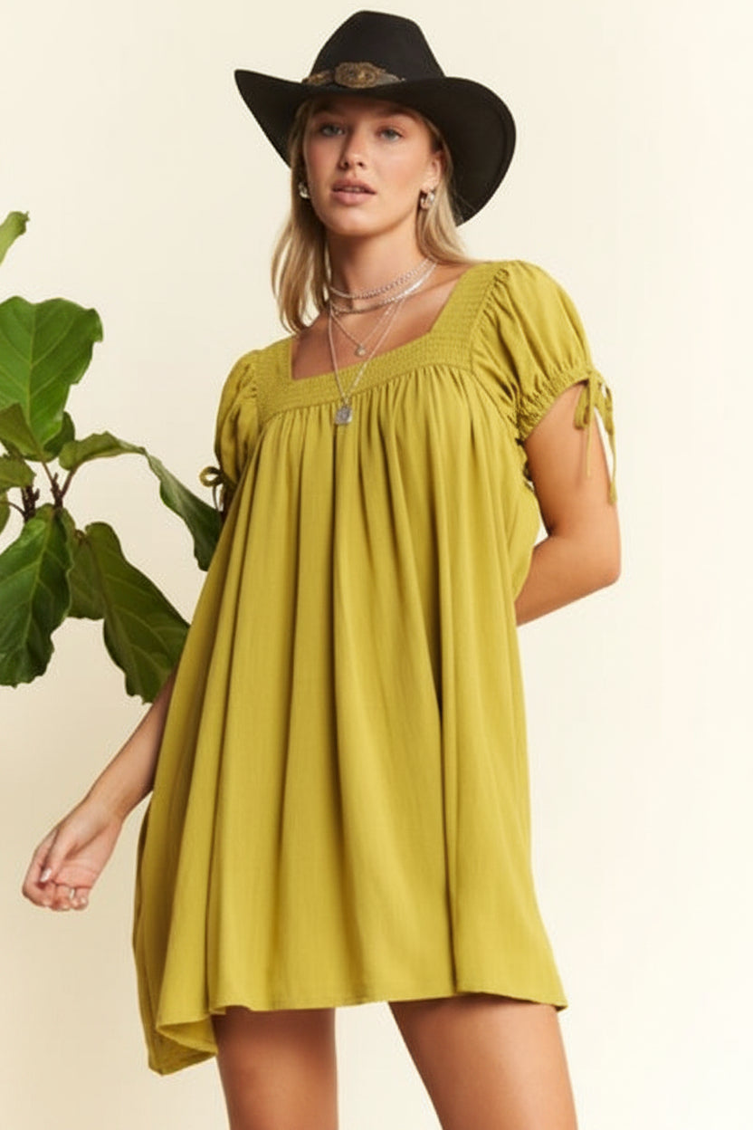 Woman wearing a yellow dress and black hat with a plant in the background