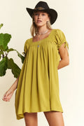 Woman wearing a yellow dress and black hat with a plant in the background